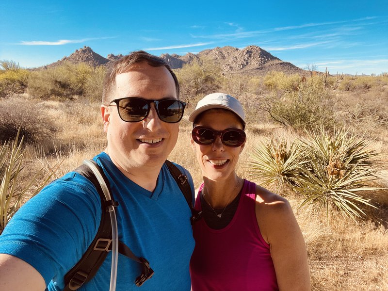 Matt and Julie on a desert hike in the McDowell Sonoran Preserve, Scottsdale, Arizona — saguaro cacti and red-rock terrain behind them