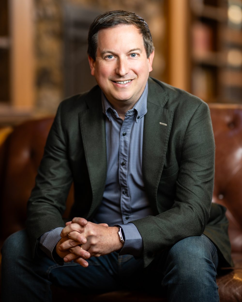 Matt Briney portrait, seated on a leather sofa in a wood-paneled library
