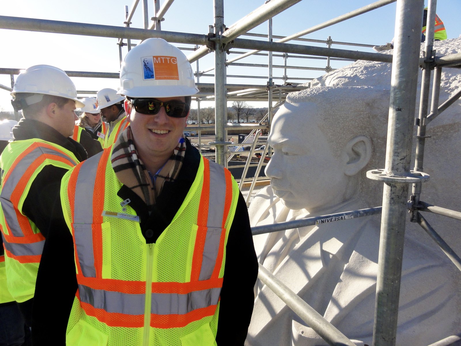Matt Briney on the MLK Memorial construction site in December 2010, wearing a hard hat and high-visibility vest, standing on the scaffolding beside the still-being-carved face of Dr. King