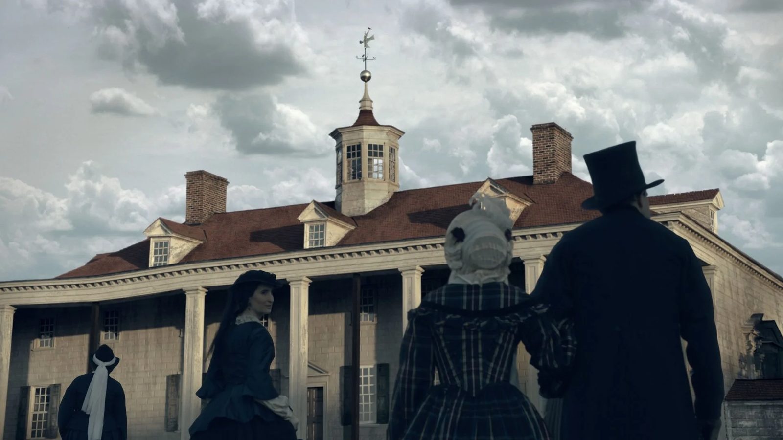Period-costumed visitors silhouetted in front of the Mansion under dramatic clouds — depicting the MVLA preservation era