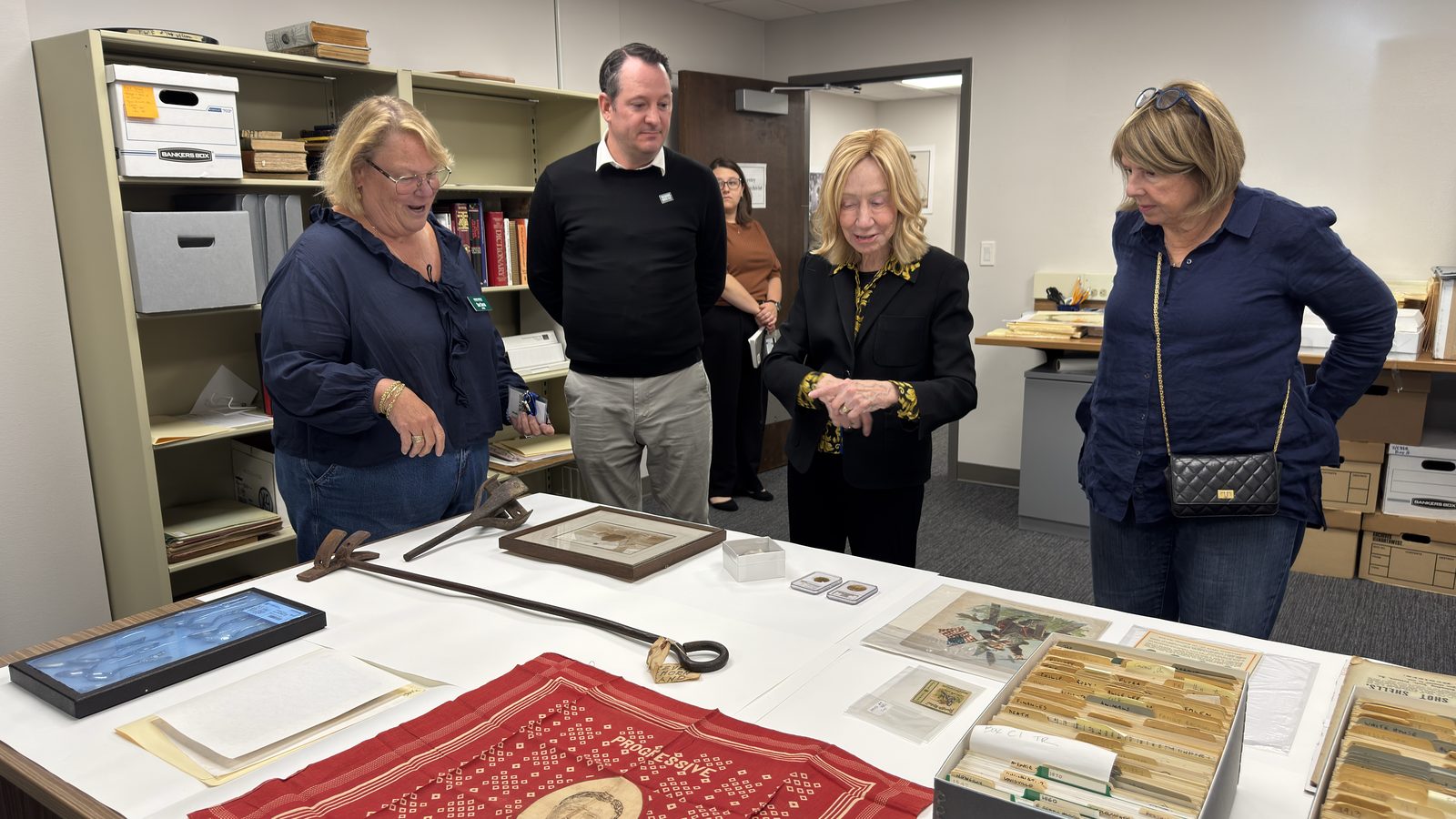 Doris Kearns Goodwin and Library staff examining Roosevelt artifacts laid out on a table in the collections workroom, including a 1912 Progressive Party battle flag