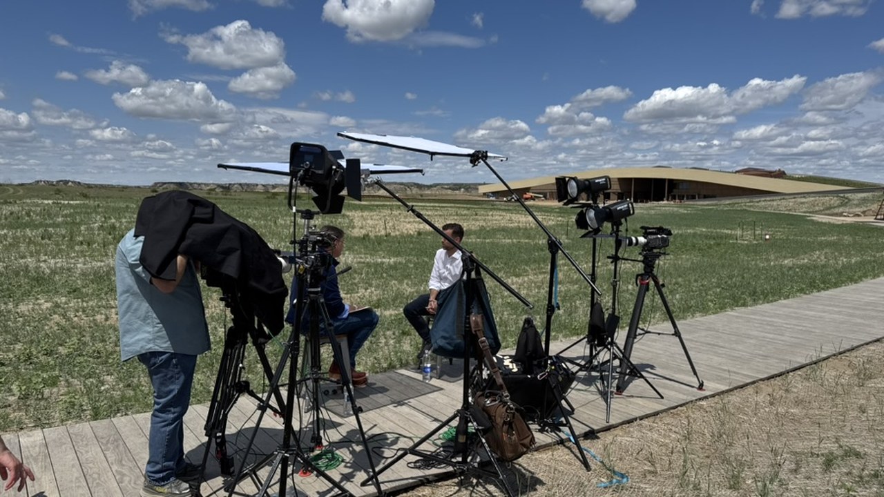 A full broadcast interview rig — cameras, lights and diffusion on stands — set up on the boardwalk with the Library in the distance