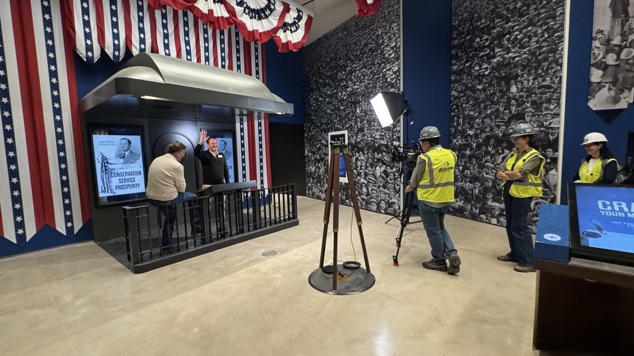 A broadcast crew in hard hats and high-visibility vests filming inside the permanent exhibition before completion
