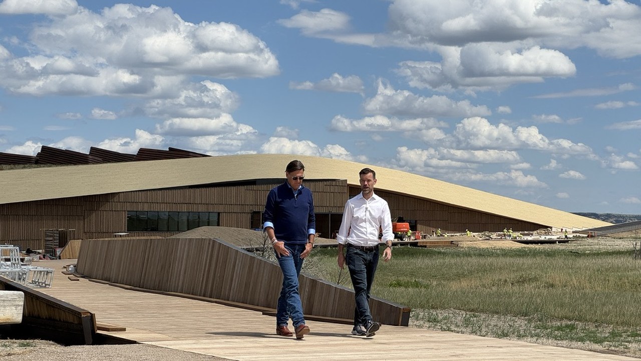 Two people walking the boardwalk toward the camera with the Library's planted roof rising behind them